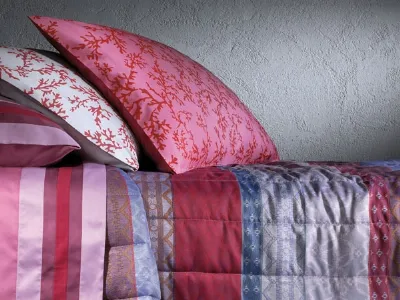 dettaglio copriletto, lenzuolo e cuscini in raso dalle fantasie floreali e a righe nei toni del rosa, rosso, bianco e azzurro